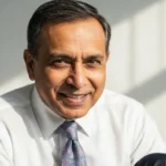 Professional businessman smiling, wearing a white shirt and tie, in a bright office setting.